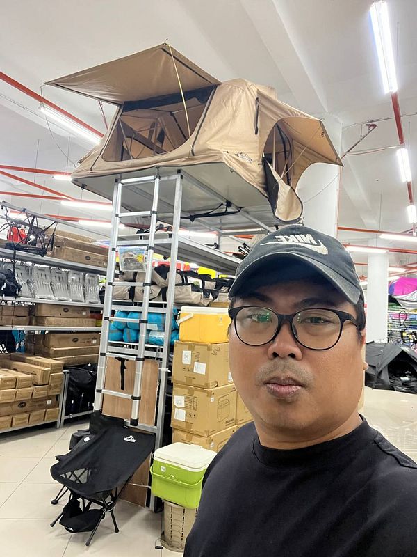 A person stands in a store with a rooftop tent displayed above them.