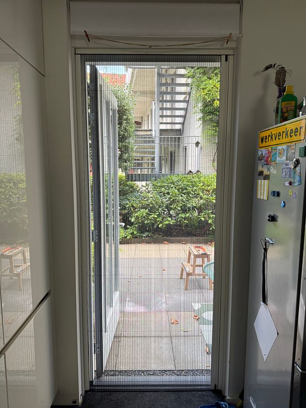 A newly fitted screen door with a metal frame installed in a house entrance.