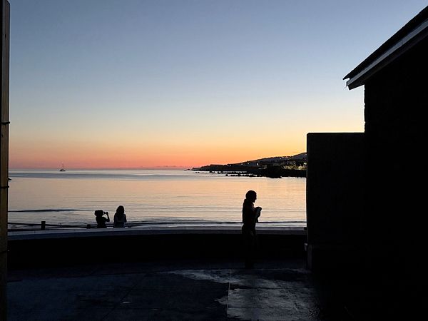 A serene sunset view over a calm sea with silhouettes of people enjoying the moment.