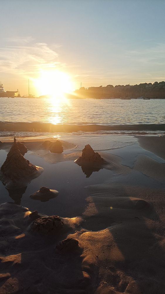 A serene beach scene at sunset with sand formations and calm water.