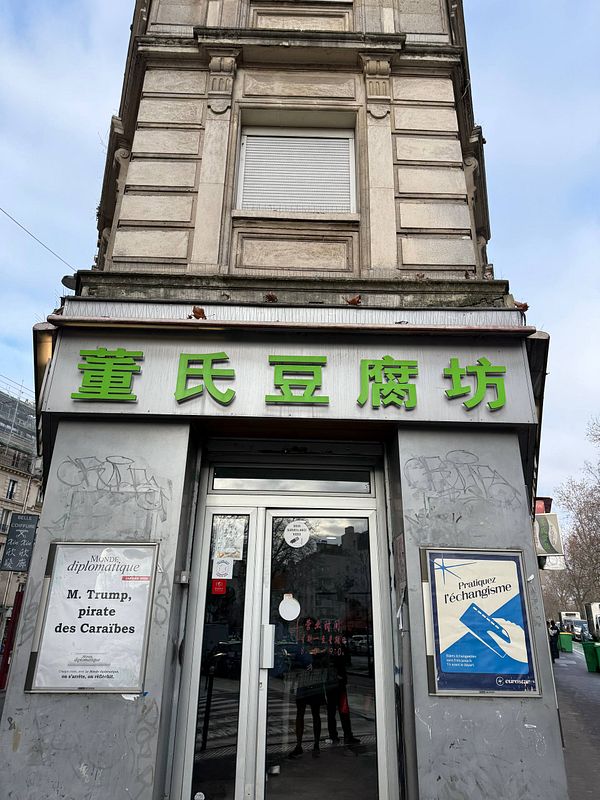 Interior of a local Chinese breakfast spot featuring a white refrigerator, a food warming cabinet, and a small table with stools.