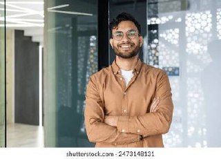 A smiling man stands confidently with his arms crossed in a modern indoor setting.