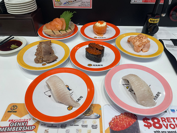 A sushi meal featuring diverse sushi pieces on colorful plates with menus and condiments on a sushi bar counter.