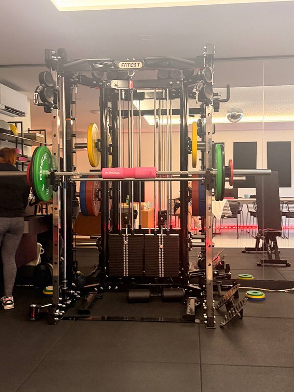 A person wearing a fitted gray athletic shirt and black workout shorts is standing in a gym environment with a large window and modern workout equipment.