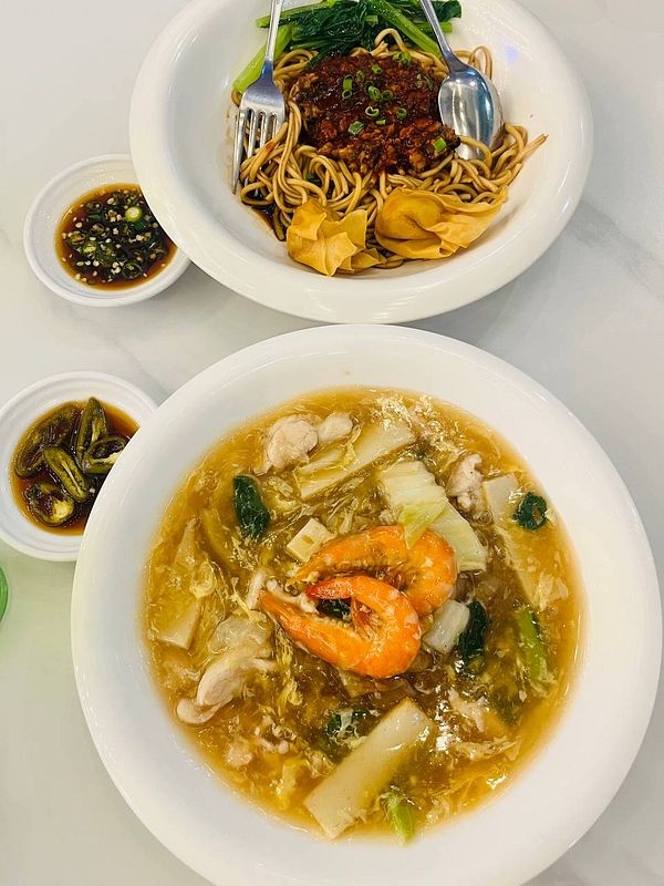 The image features two bowls of Asian cuisine, one with noodles and the other with a seafood and vegetable broth.