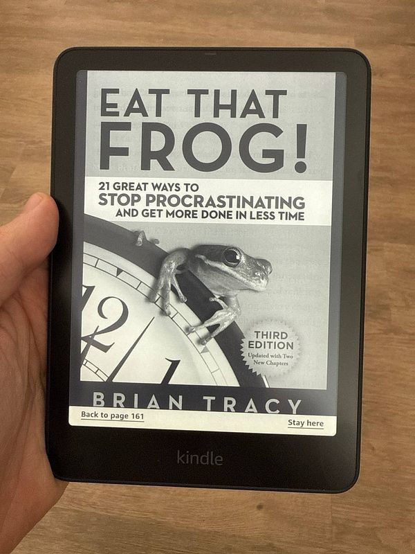 A Kindle device displays the cover of 'Eat That Frog!' by Brian Tracy.
