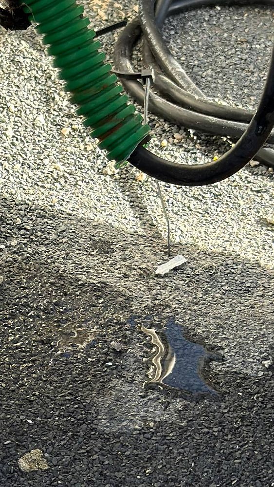 A close-up view of a green and black electrical tube on a rooftop, with water pooling around it.