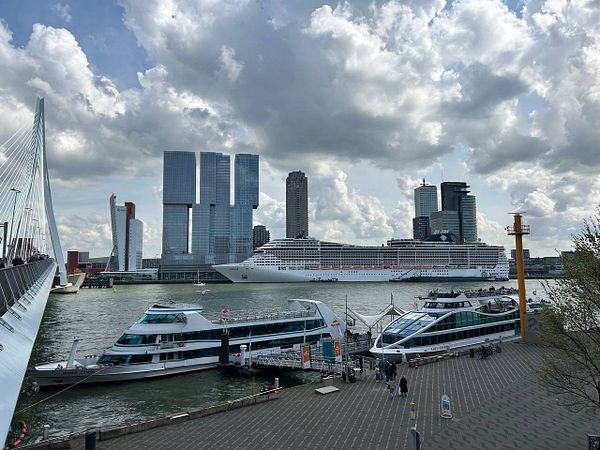 A scenic view of Rotterdam's waterfront featuring modern architecture and a large cruise ship.