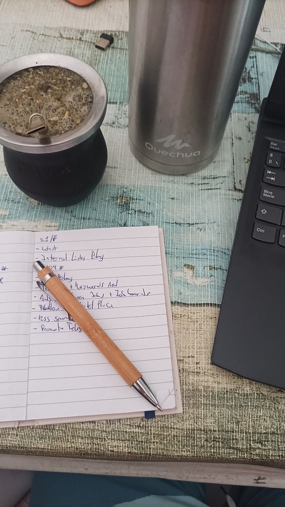 A workspace setup featuring a notebook, a pen, a mate cup, a thermos, and a laptop.