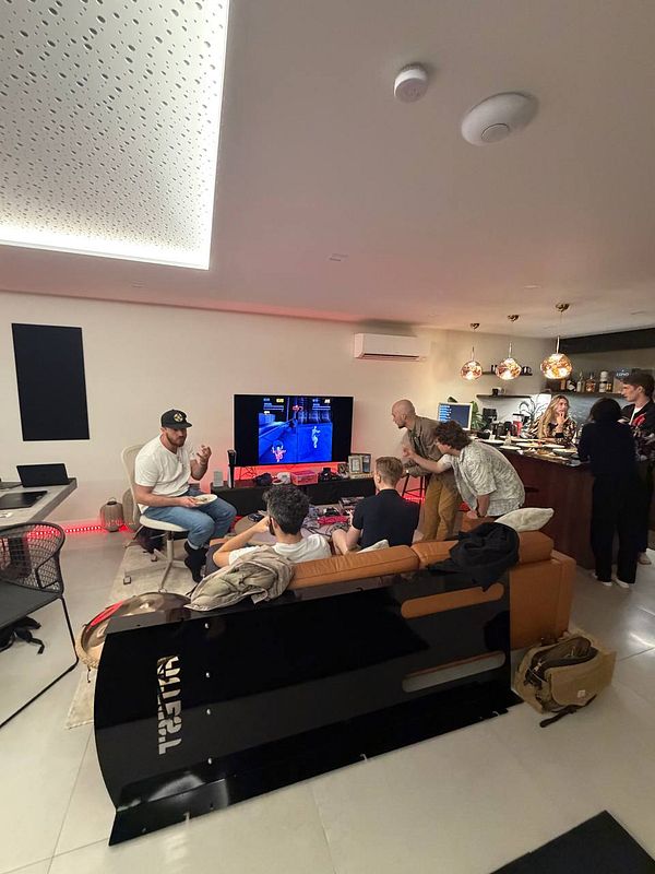 A group of people in a modern living room setting playing video games and socializing near a kitchen area.
