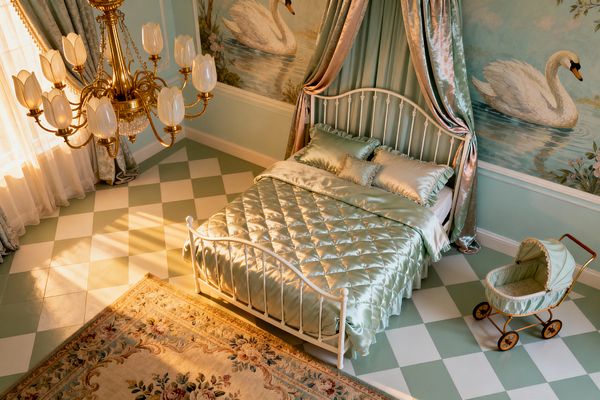 A children’s bedroom in mint and ivory features a white wrought-iron bed with quilted satin bedding beneath a draped velvet canopy. Hand-painted swan murals line the walls, a brass chandelier with tulip-shaped glass shades hangs overhead, checkerboard floor tiles and a floral wool rug ground the space, and a vintage mint pram stands nearby as sunlight filters through sheer curtains, casting a warm, nostalgic glow.