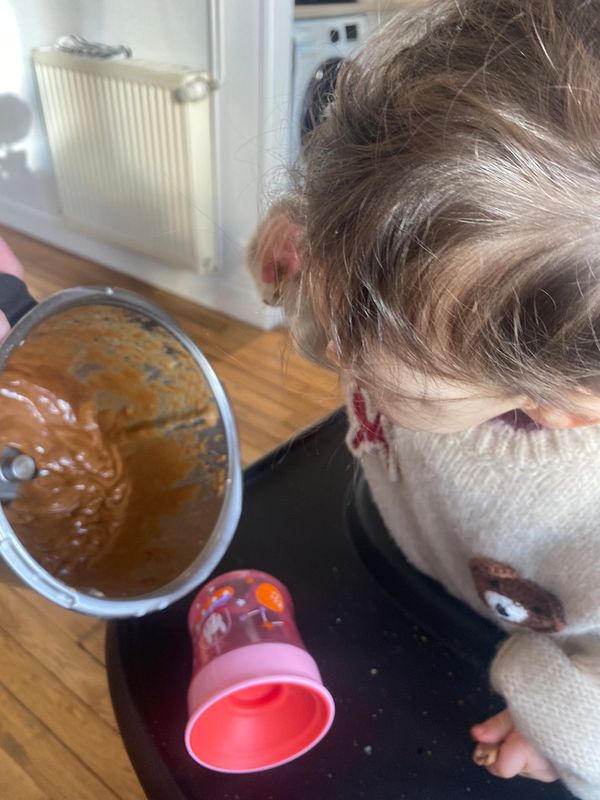 A jar of speculoos paste with a spoon and fresh ginger on a yellow cloth with other food items.