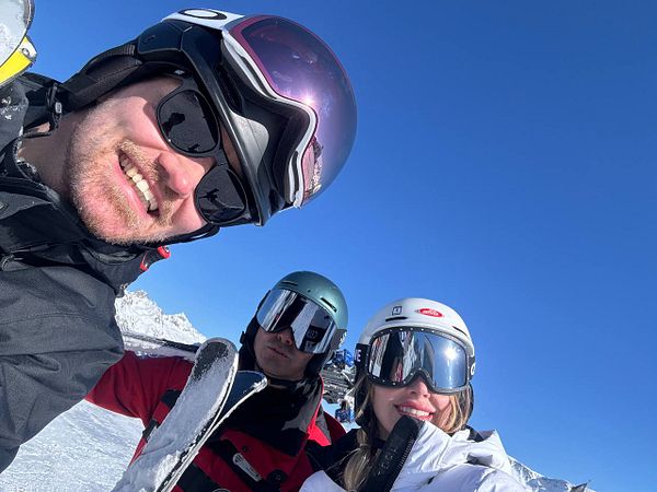 A group of three friends poses for a selfie while skiing on a sunny day.