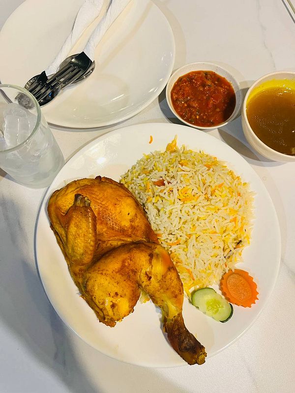 A plate of chicken mandi rice with side dishes and utensils.