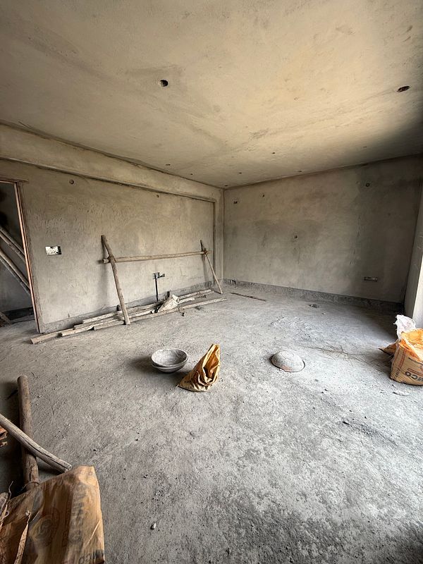 An unfinished room with bare walls and a concrete floor, featuring construction materials and tools.