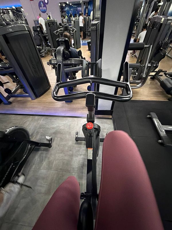 An active woman wearing athletic wear is lifting dumbbells in a gym setting with brick walls and large windows.