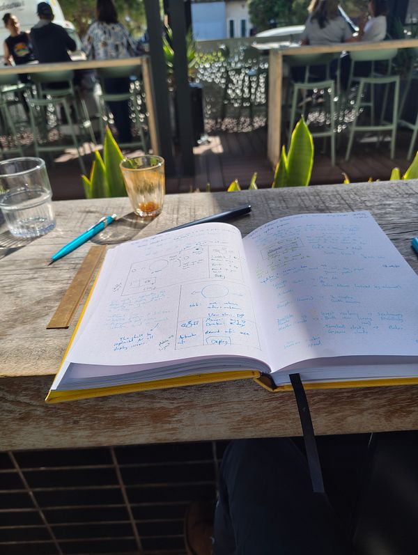 A person is sketching designs in a notebook at an outdoor café after a bike ride.