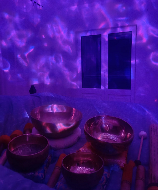 A serene setup for a sound bath featuring various singing bowls and a calming purple light ambiance.