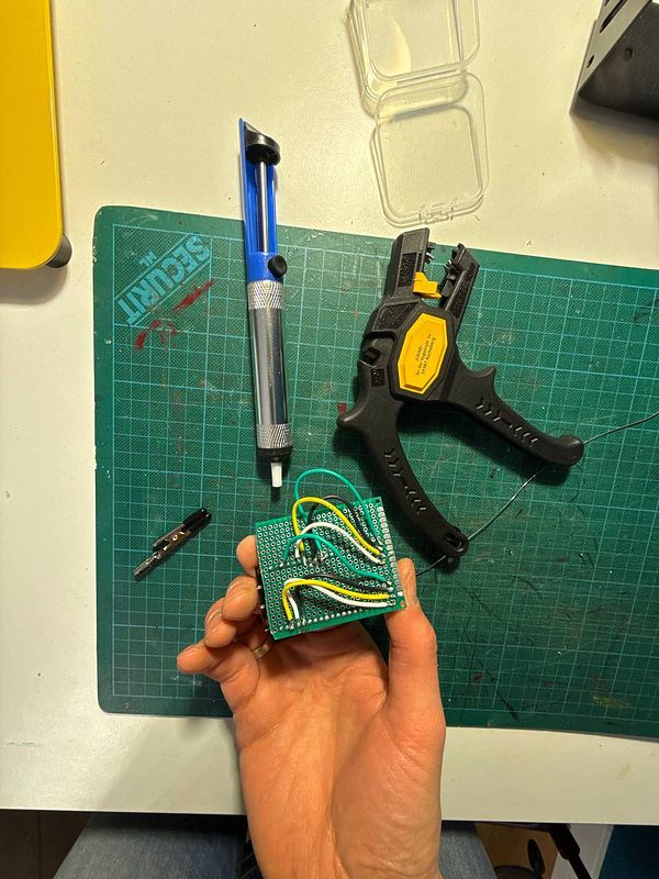 A hand holds a completed electronic circuit on a green prototyping board surrounded by various tools.