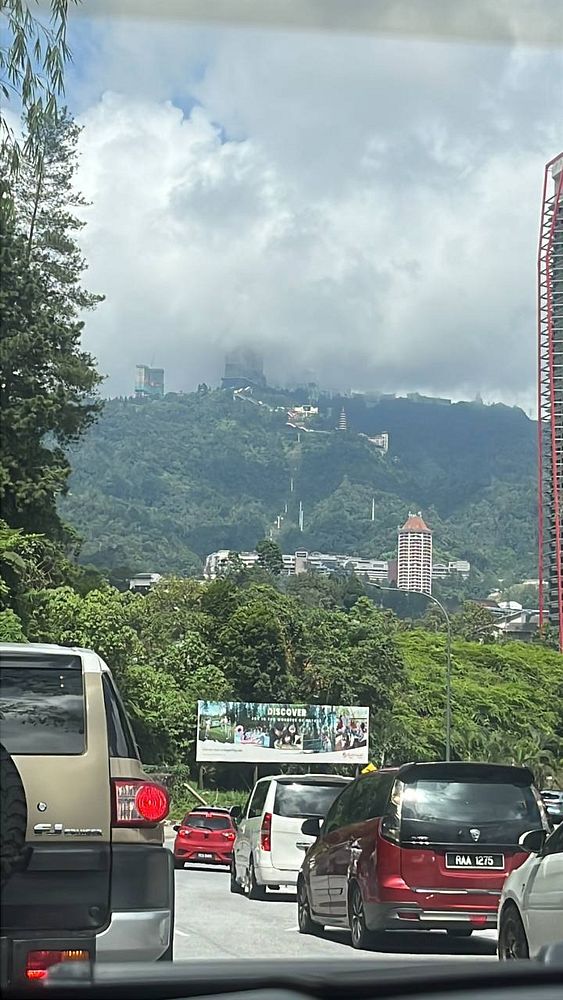 A long line of vehicles congested on a winding mountain road amidst dense forest at Genting Highlands.