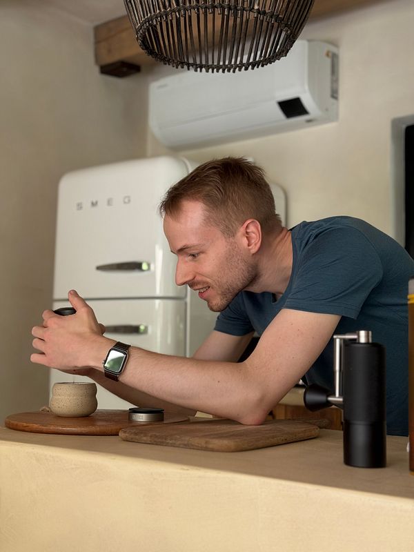 A man is preparing coffee using a portable grinder and espresso maker in a cozy kitchen setting.