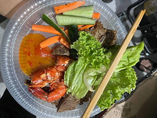 A plate of grilled food featuring shrimp, beef, fresh vegetables, and dipping sauce.