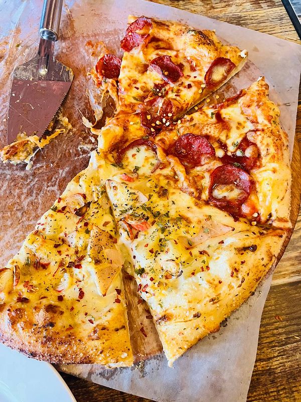 A delicious pizza with various toppings is partially sliced and served on a wooden table.