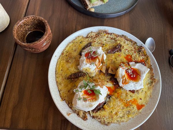 A delicious brunch plate featuring poached eggs on a savory base, accompanied by a traditional drink.