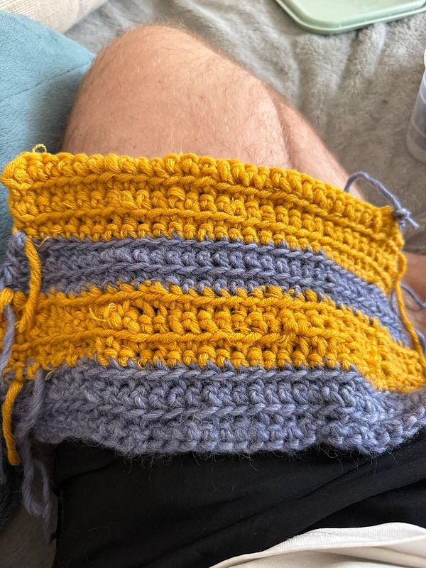 A crocheted piece in yellow and blue yarn rests on a person's leg.