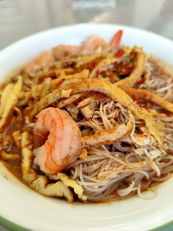 A bowl of Sarawak laksa featuring thick broth, prawns, shredded egg, and vermicelli noodles.