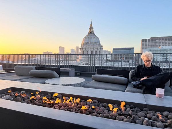 View of a San Francisco rooftop with a person reclining and the city skyline in the background under a clear sky.