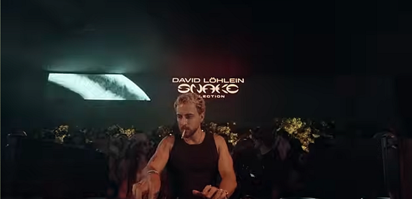 David Löhlein performing live in a dimly lit environment with projected text behind him.