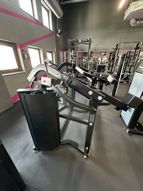 The image features a gym interior with a focus on a specific piece of strength training equipment.