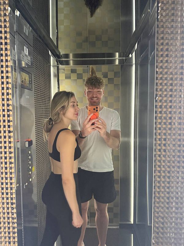 A man and a woman taking a mirror selfie in an elevator with patterned walls and reflective surfaces.