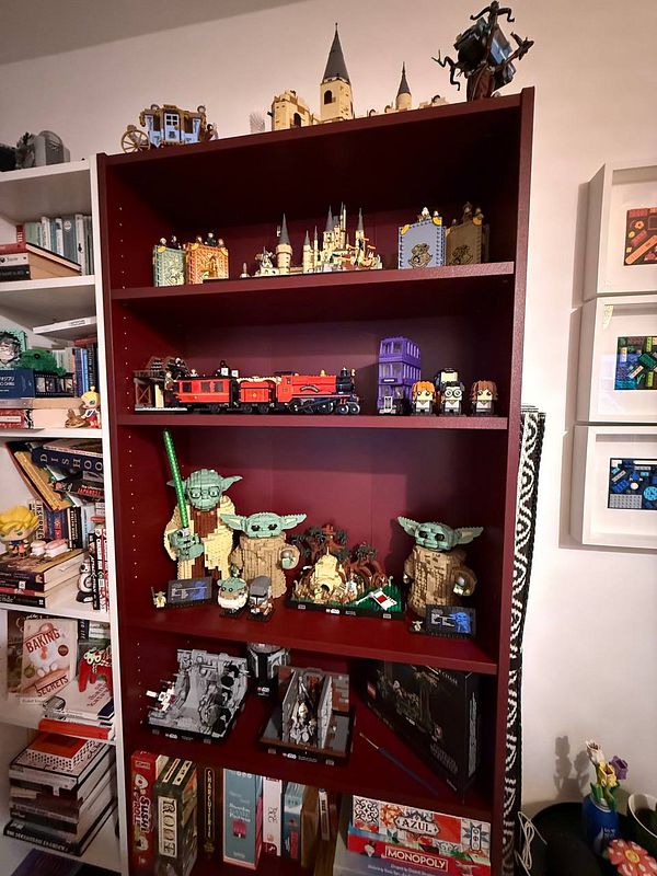 A colorful display of various Lego sets arranged on a maroon bookshelf.