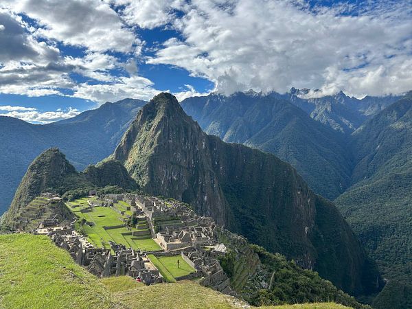 A scenic view of the ancient Machu Picchu archaeological site nestled among lush green mountains under a partly cloudy sky.