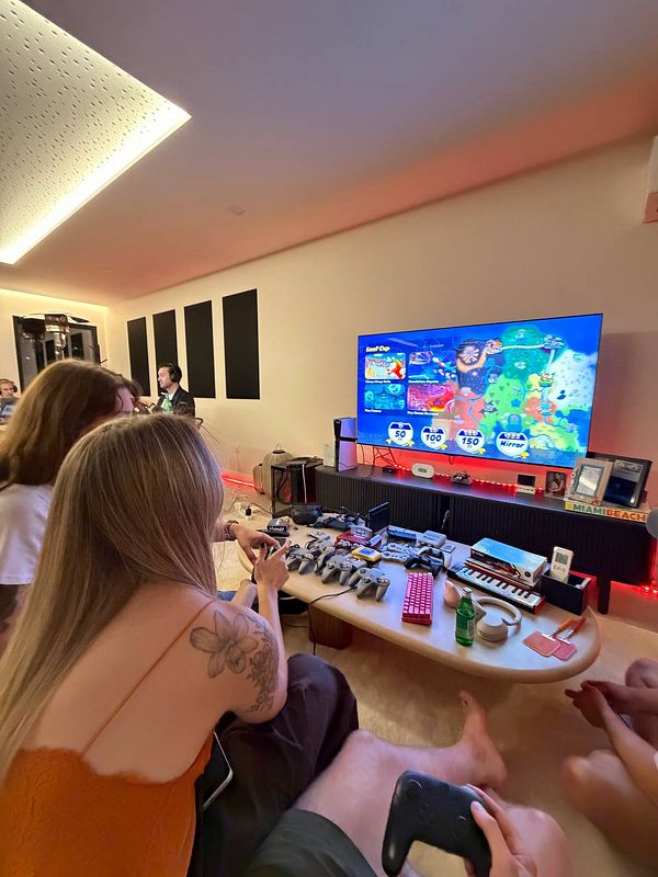 Two people playing a video game on a large TV in a cozy room with multiple gaming controllers and musical equipment on the table.