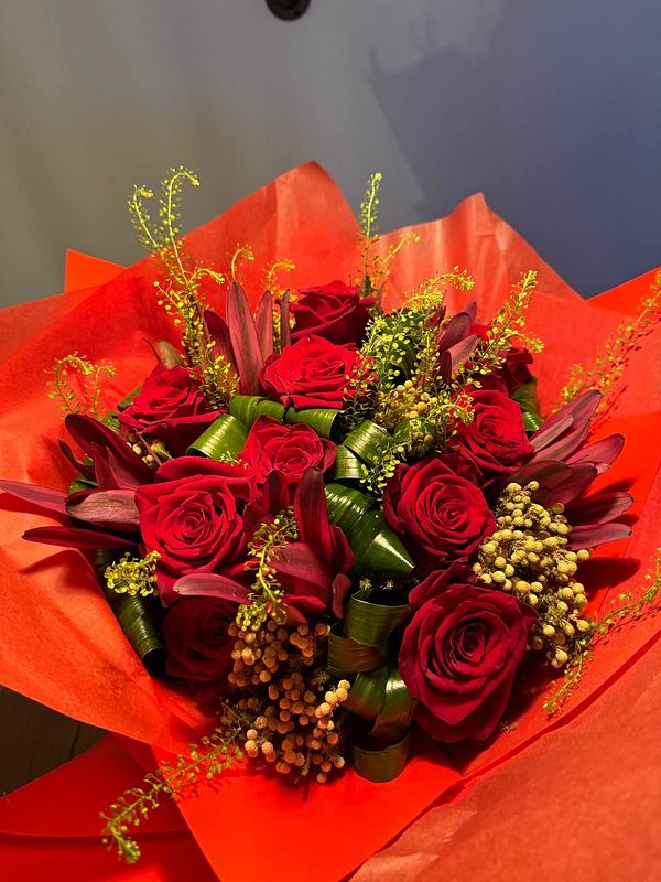 A vibrant bouquet of red roses and assorted greenery is beautifully arranged in bright orange wrapping.