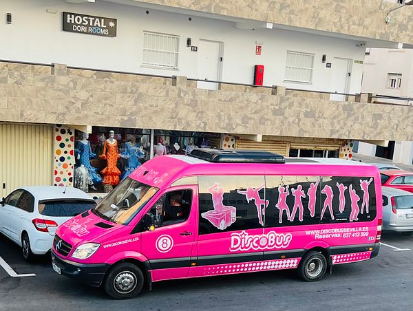 A vibrant pink party bus is parked in front of a clothing store in a beach town.