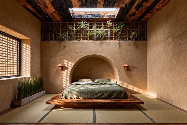 A serene biophilic bedroom centers on a low walnut platform bed with olive linen, tucked into an arched niche within clay-plaster walls. Tatami flooring, terracotta mushroom sconces, a charred-wood ceiling with a skylight, and a wood trellis planted with air plants create a natural setting, while a concrete planter of tall grasses and a lattice-screened window cast dappled light across the room.