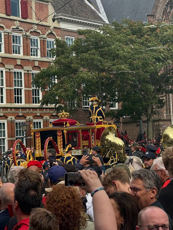 A crowd gathers to witness a royal carriage procession.