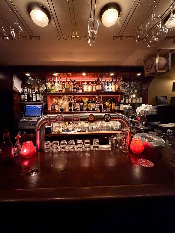 Interior of a pub or café with brown leather chairs and tables featuring glasses filled with beer and coaster pads.
