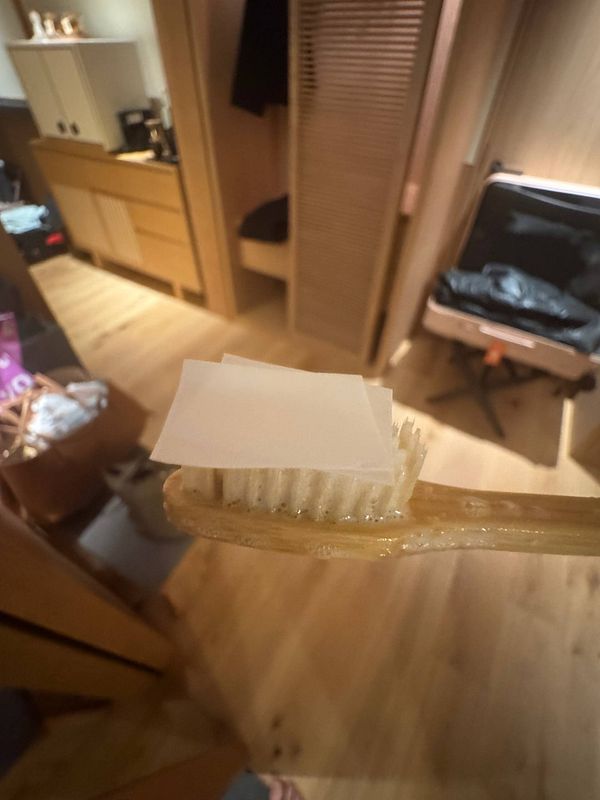 A toothbrush holds eco-friendly toothpaste paper in a hotel room setting.