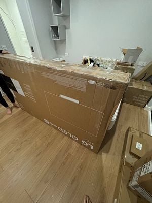 A large, boxed LG 77" OLED TV is being prepared for return in a cluttered room.