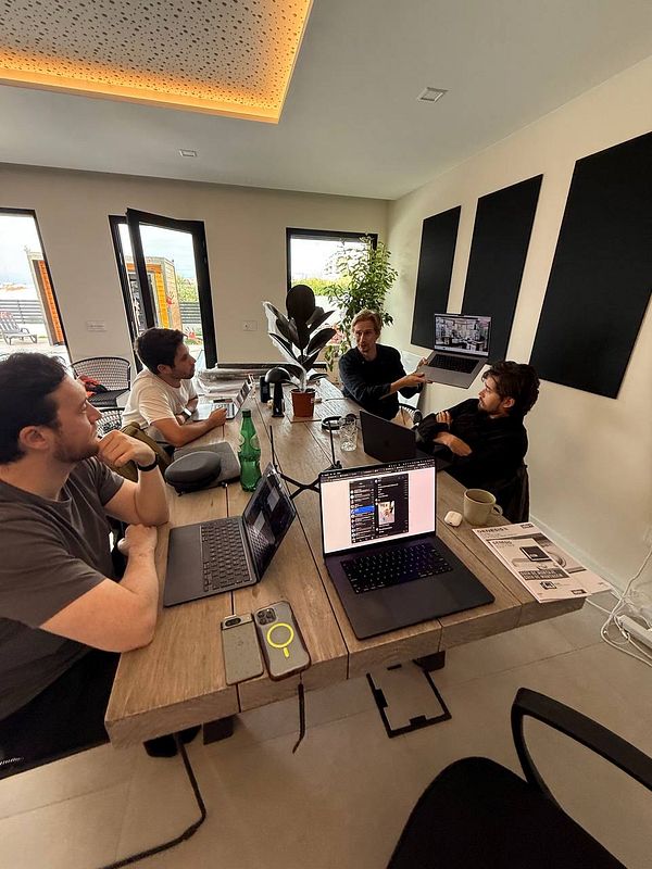 A group of four individuals is engaged in a coworking session around a wooden table in a modern workspace.