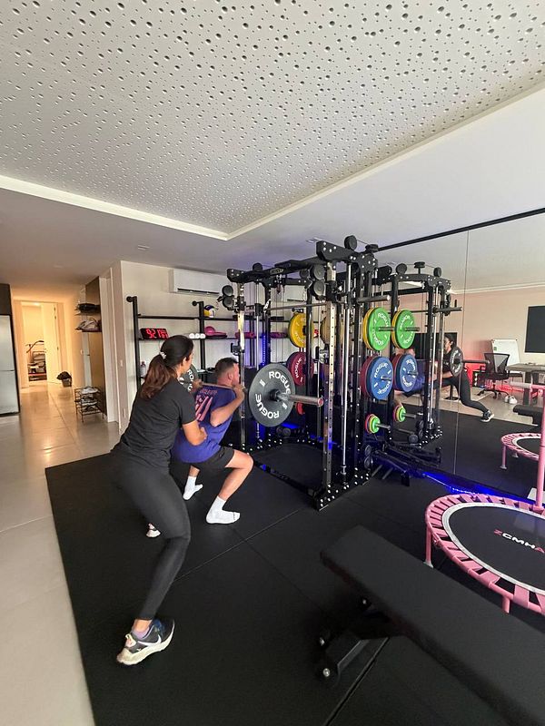A photograph of a person at a gym, lifting weights while wearing a tank top and shorts.