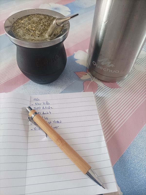 A cozy workspace featuring a traditional mate drink, a notebook with tasks, and a thermos.