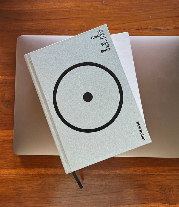 A book titled 'The Creative Act: A Way of Being' by Rick Rubin is placed on a wooden surface next to a laptop.
