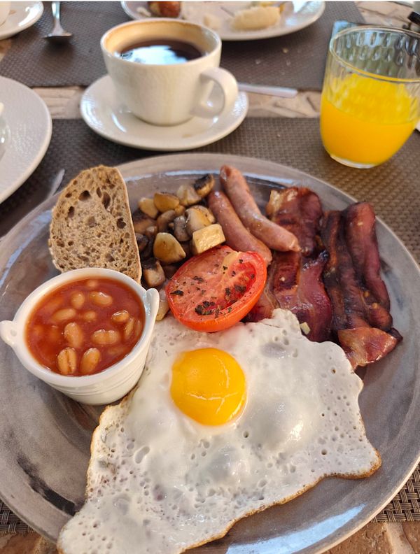A spread of breakfast items including a coffee cup, smoothie, toast, fruit, and croissants on a wooden table.