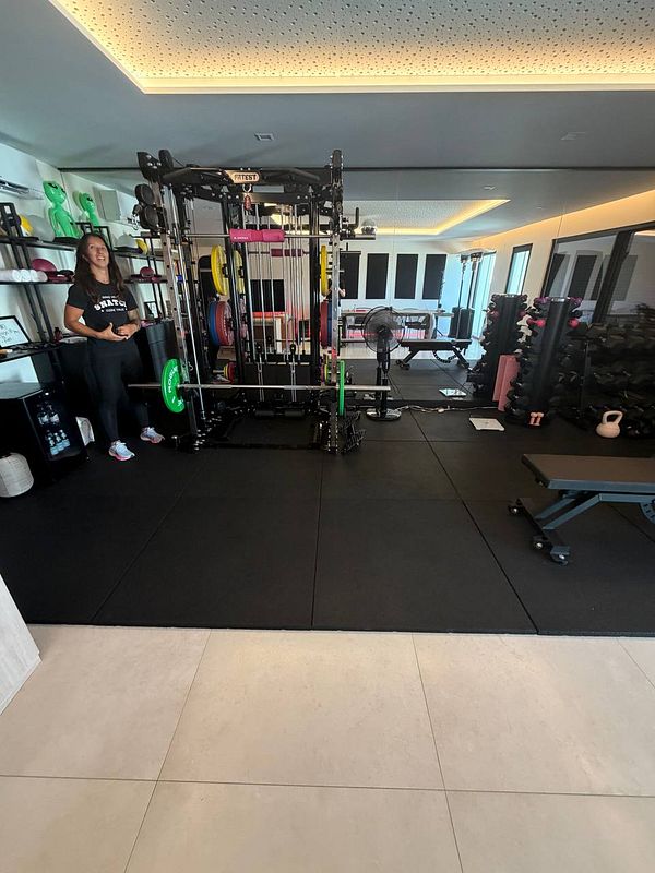 Full-length portrait of a muscular man exercising with gym equipment in a bright, spacious gym.